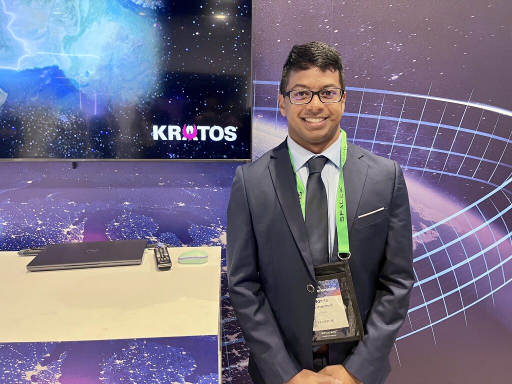 Dawn Zoldi/P3 Tech Consulting Professional man in a dark suit with tie at a space-themed expo booth, wearing a green lanyard and exhibitor badge.