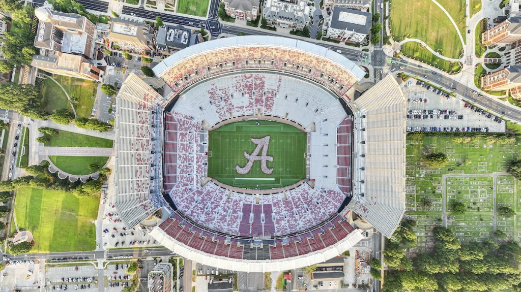 D-Fend Solutions Aerial view of a large football stadium with a big 'A' logo on the green field and surrounding seating stands and streets nearby.