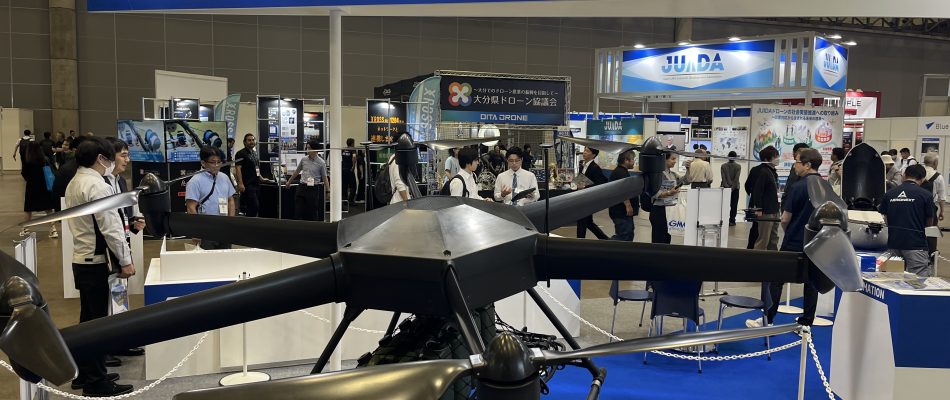 Exhibition hall with a large Topia banner overhead and people viewing drone displays below.