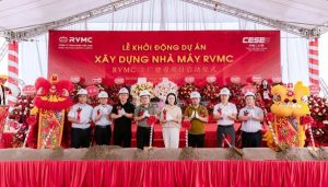 Officials in hard hats and formal dress perform a groundbreaking ceremony on a red stage backdrop for the RVMC project, flanked by lion dance figures.