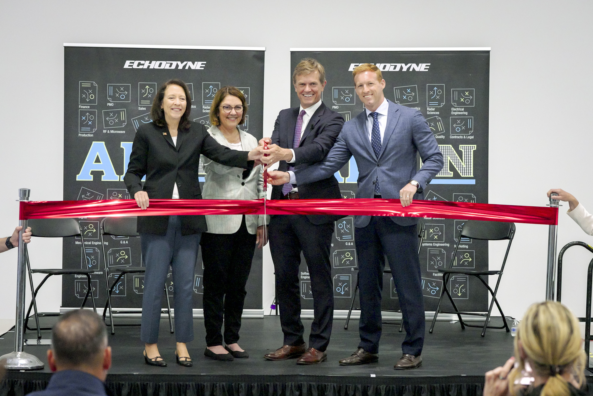 Four professionals in business attire cut a red ribbon at a corporate ribbon-cutting ceremony, with Echodyne banners in the background.