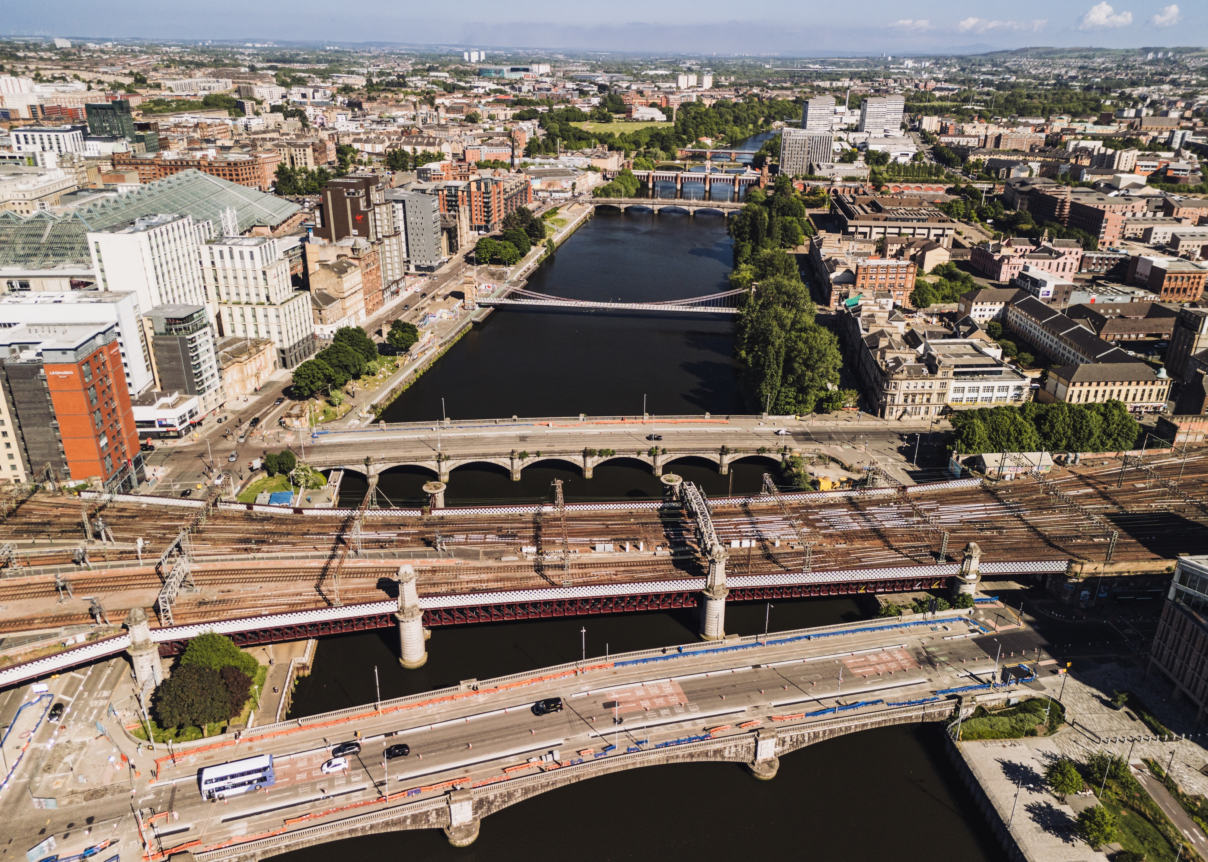 Aerial cityscape showing a wide river with several bridges, dense buildings along the banks, and railway tracks in the foreground.